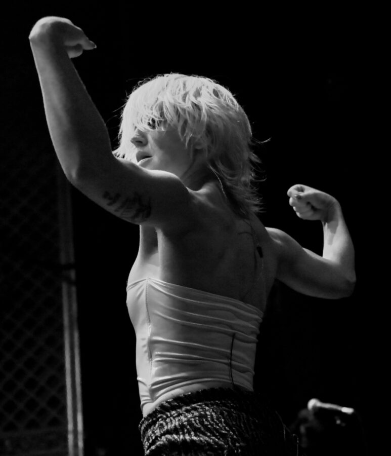 Amy Taylor of Amyl and The Sniffers without her back to the crowd flexing her biceps.